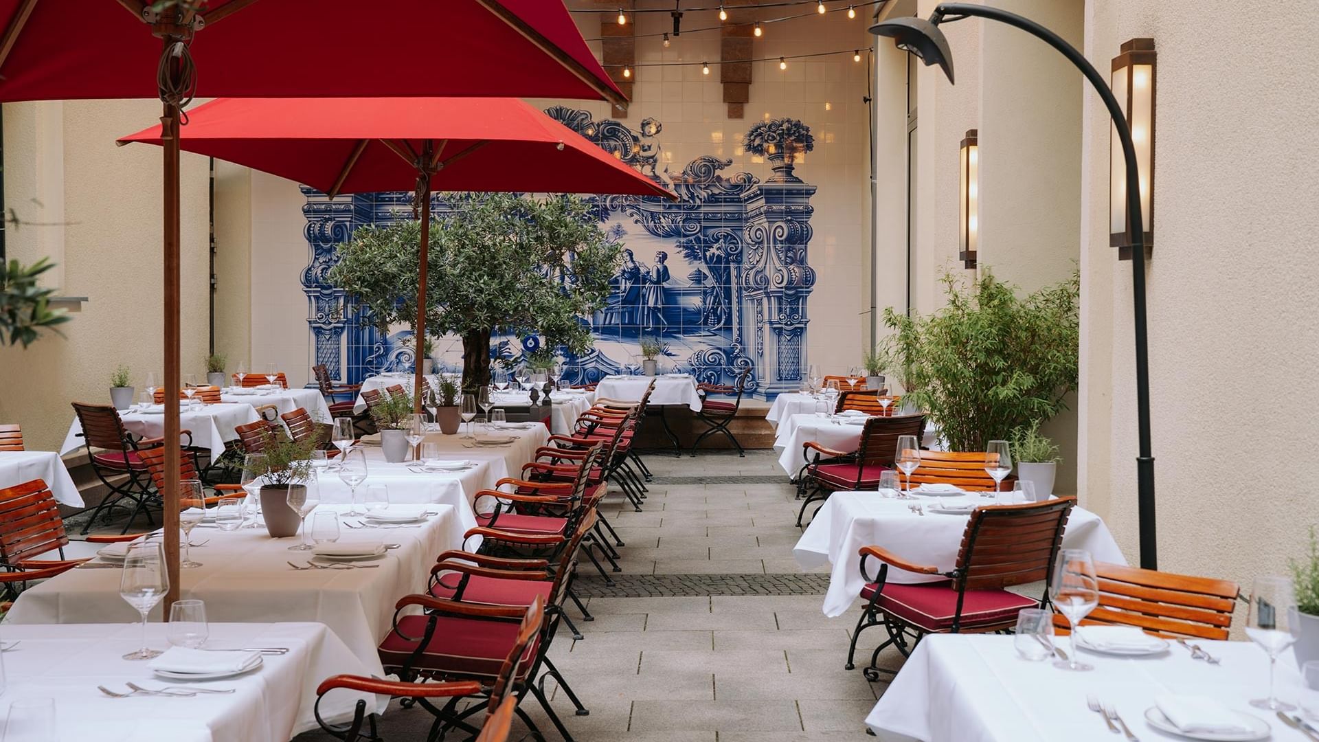 Outdoor courtyard dining area with red umbrellas and blue decorative tile mural at Titanic Gendarmenmarkt Berlin