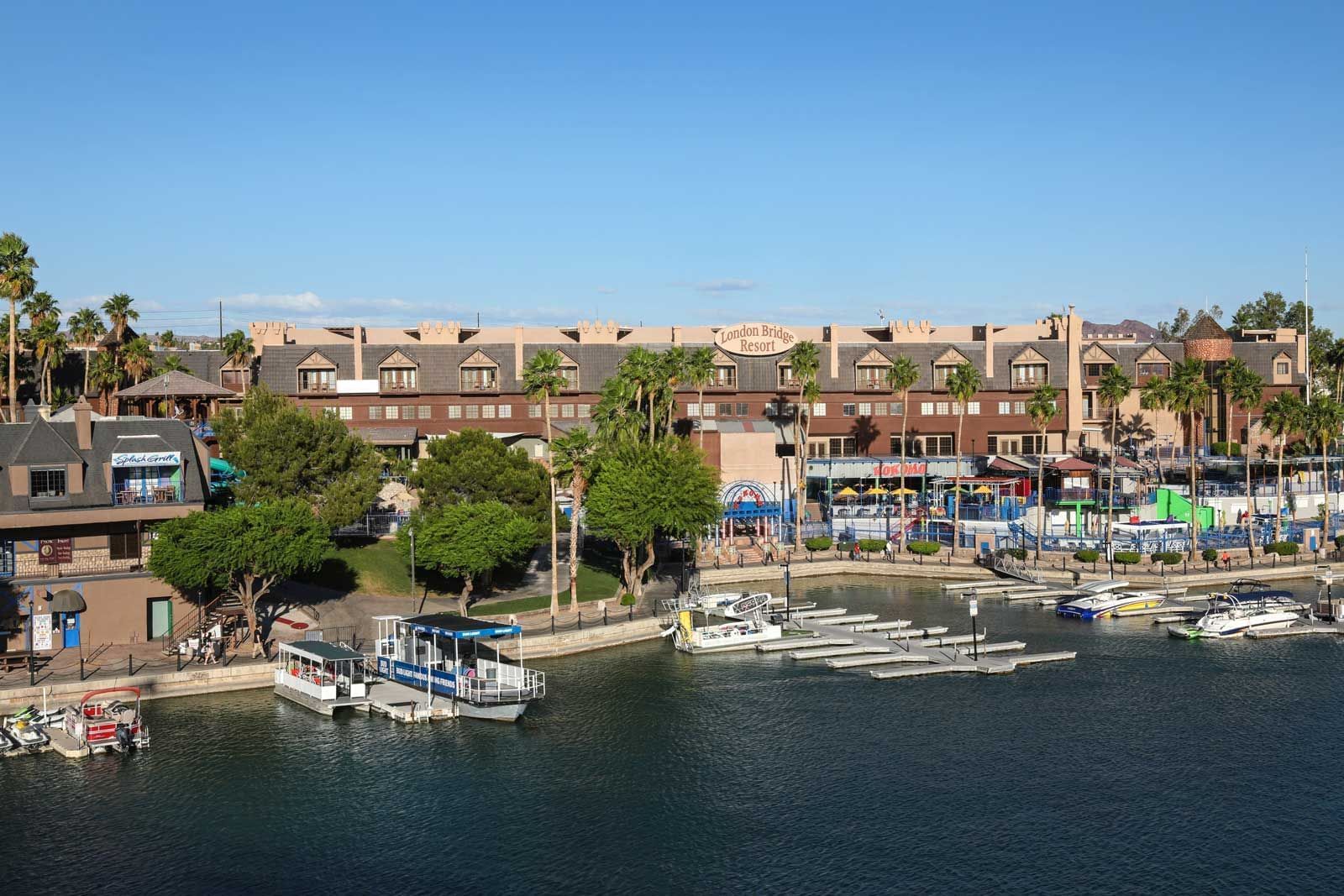 Waterfront view of resort buildings with marina, boats, palm trees, and shops along the shoreline at London Bridge Resort