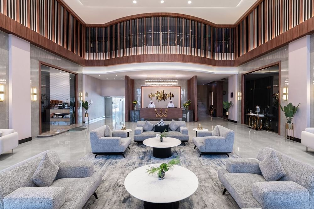 Grey plush chairs and round marble tables surrounding a large rug in a lobby at Warwick Al Jubail