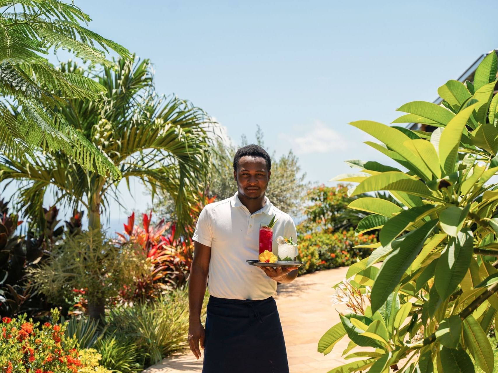 Waiter holding a colorful drinks tray in the lush garden of Breeze Restaurant at Golden Rock Resort