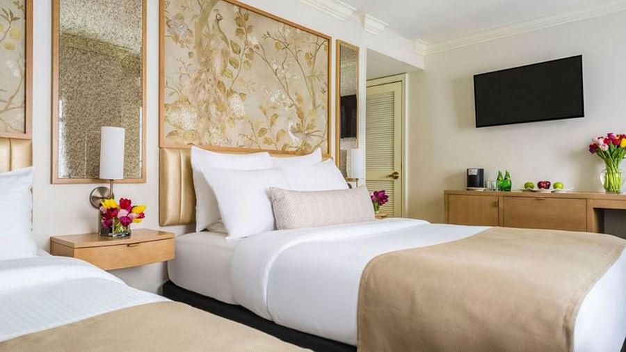 Bed with side tables near a wood cabinet under a hanging TV in Two Queen Beds at Warwick Allerton Chicago