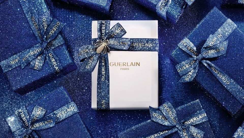 Guerlain Paris gift box with blue glitter ribbons and bee charm surrounded by gift boxes at Hotel X Toronto