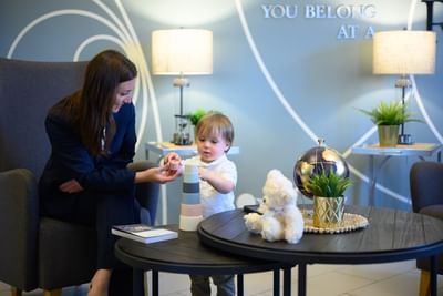 Woman and a young child playing with a block tower on a wooden coffee table in the bright lobby at Rodd Moncton