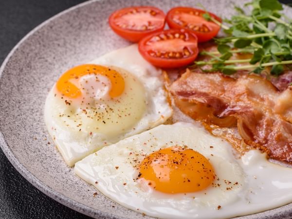 Hearty breakfast plate with fried eggs, bacon, and grilled tomatos