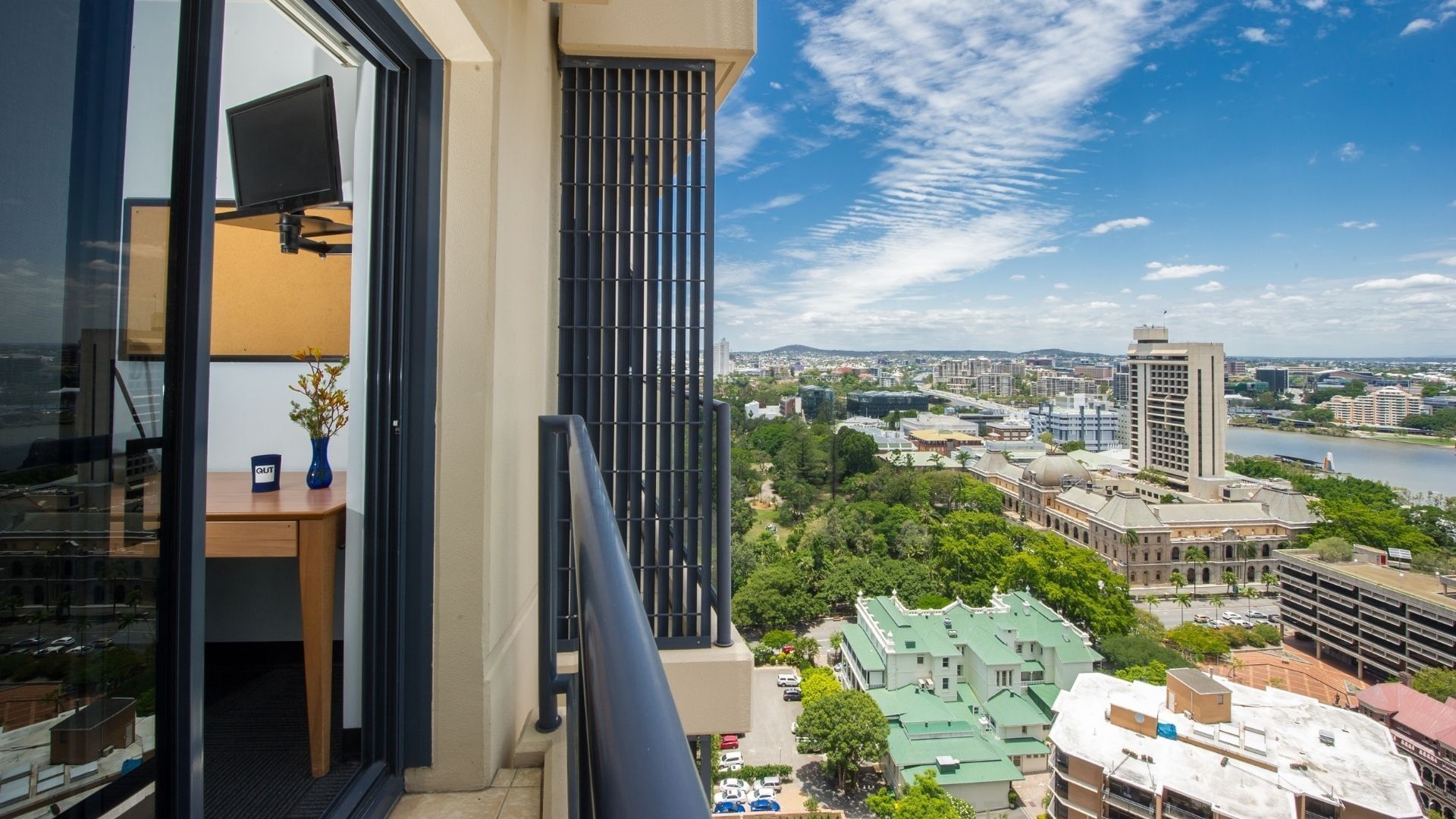 Private balcony with panoramic city and river views at UniLodge on Margaret, featuring modern glass doors and urban skyline.