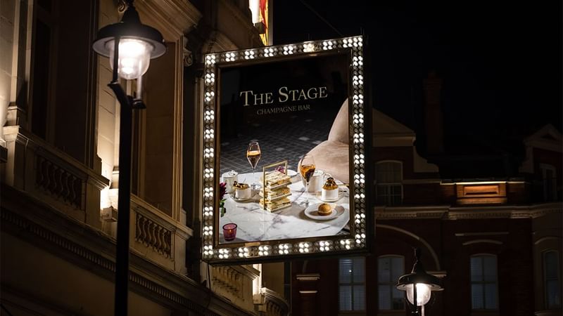 Illuminated marquee style billboard for The Stage Champagne Bar at night.
