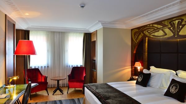 Red velvet chairs by a small table surrounding a bright window in Deluxe Room at Warwick Ankara