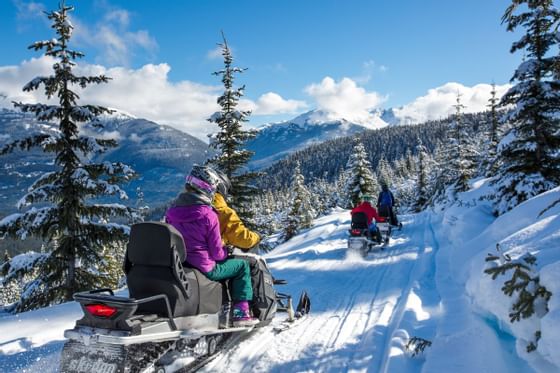 People riding snowmobiles on a snowy trail near Blackcomb Springs Suites