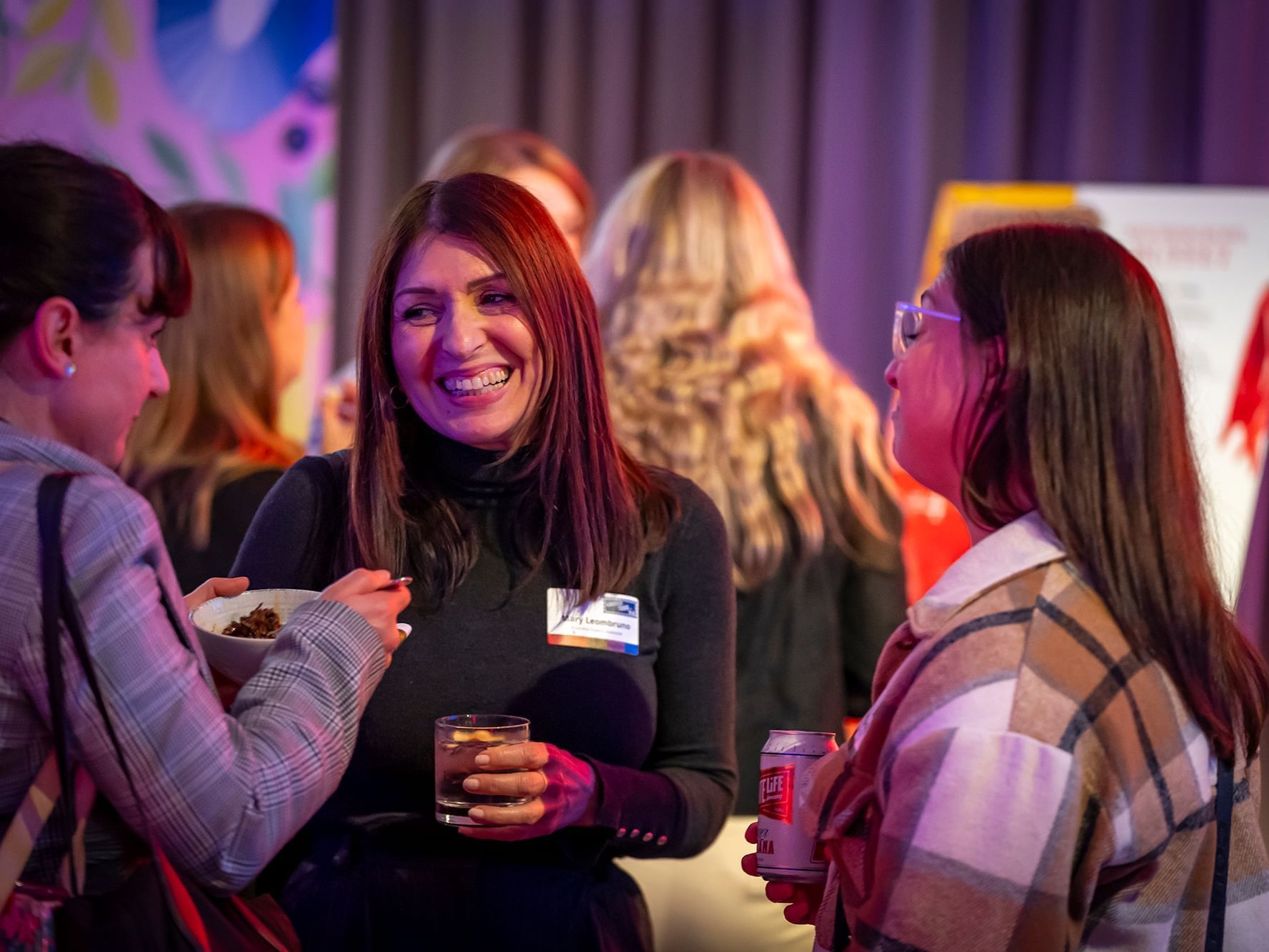 Three women chatting with food and drinks at a post meeting networking event.