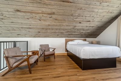 Modern bedroom with a sloped wooden ceiling, cozy bed, and two armchairs in the Villa at Off Shore Resort