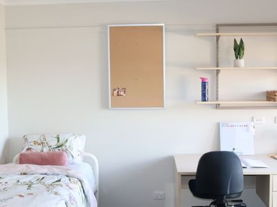 A room with a bed, desk, chair, bulletin board, shelves with items, and a calendar.