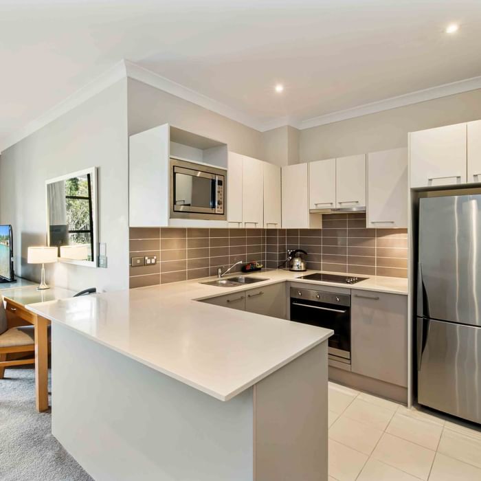 One Bedroom Apartment kitchen interior with appliances, white cabinets, and grey backsplash at Mercure Kooindah Waters