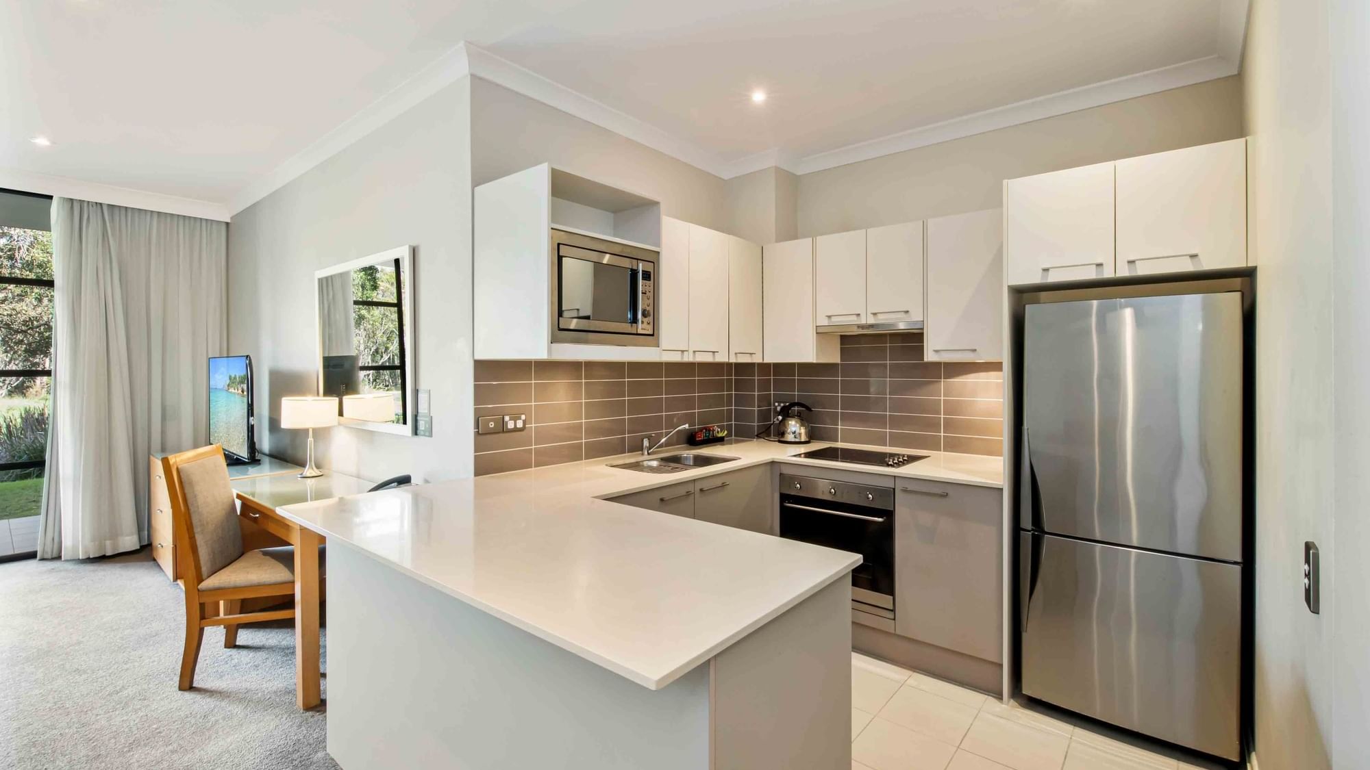 One Bedroom Apartment kitchen interior with appliances, white cabinets, and grey backsplash at Mercure Kooindah Waters