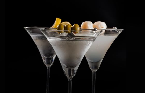 Three martini glasses with olives and lemon garnishes on a black background at Carlton Hotel Bangkok Sukhumvit