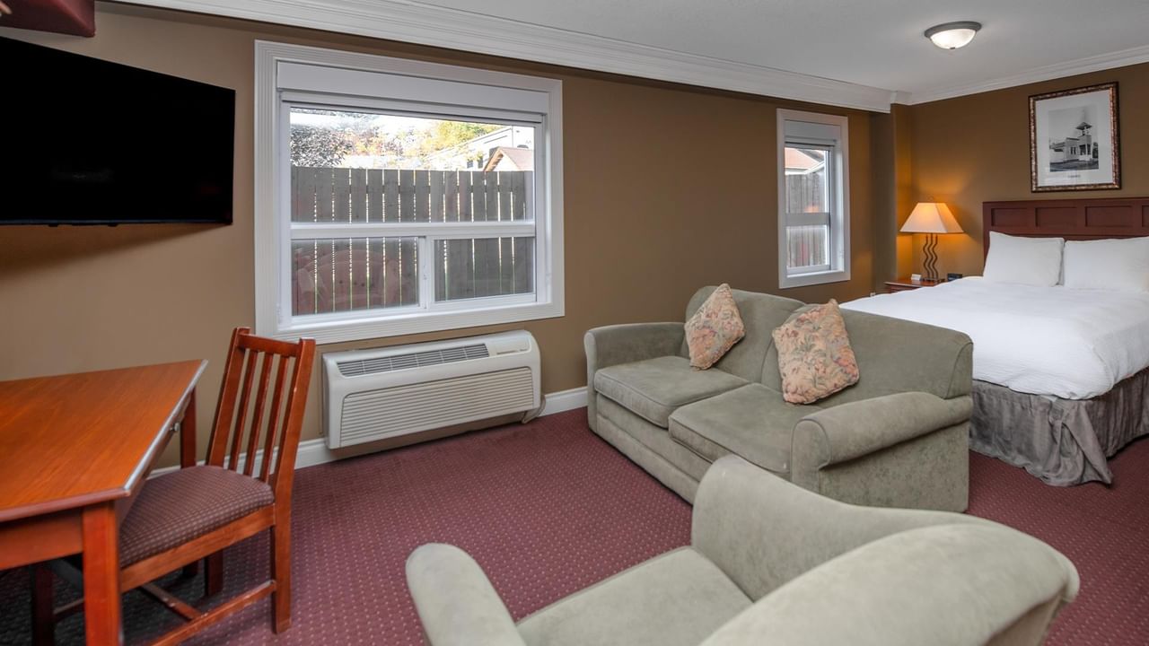 Spacious hotel room with sage green sofa, work desk, and white bedding at Coast Edson Hotel.