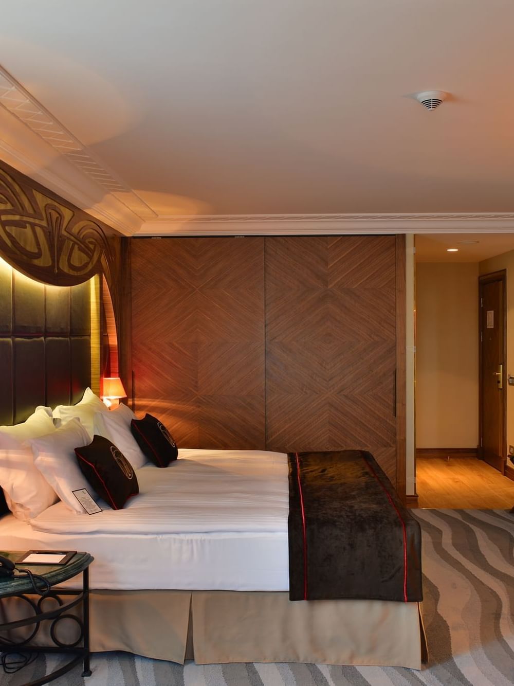 Work desk by a large bed with brown throws under a warm glowing light in Junior Suite at Warwick Ankara