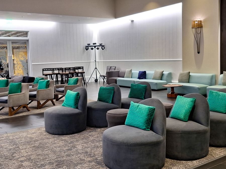 Grey armchairs with teal cushions by a long light-blue sofa under bright lights at Warwick Paradise Island Bahamas