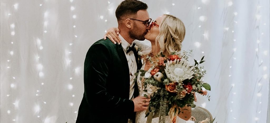 Newlyweds kissing under soft string lights at a Canmore wedding reception.