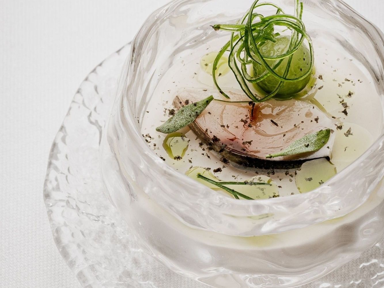 Cured fish dish with green herbs in clear glass bowl on textured plate served at Tom Brown at The Capital