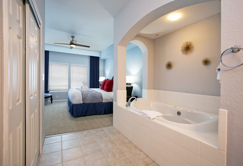 A bathroom with a large soaking tub and an archway leading to a bedroom with a bed and ceiling fan.
