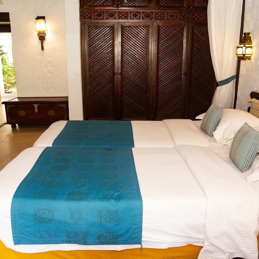 Two cozy beds with white sheets and blue blankets in a family room at Serena Beach Resort & Spa Mombasa.