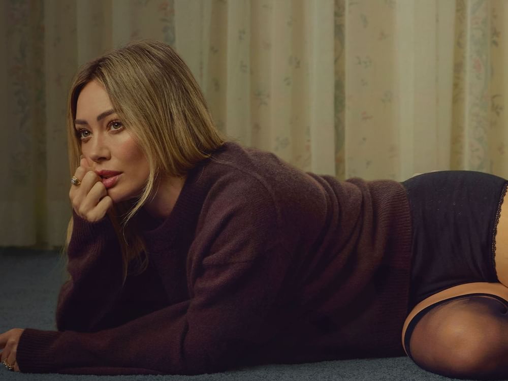 Hilary Duff lying on floor with hand on chin and a contemplative look.