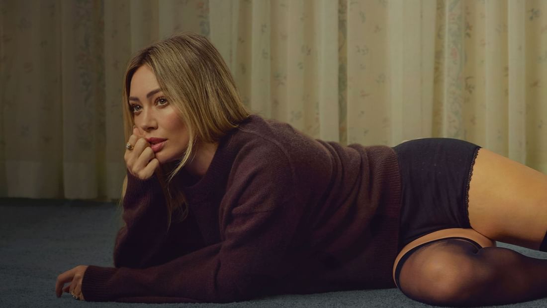 Hilary Duff lying on floor with hand on chin and a contemplative look.