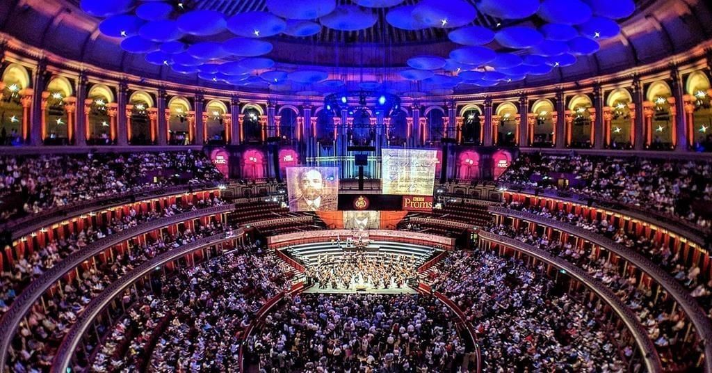 Large crowd seated in a grand hall with a stage and a large screen at The Royal Albert Hall
