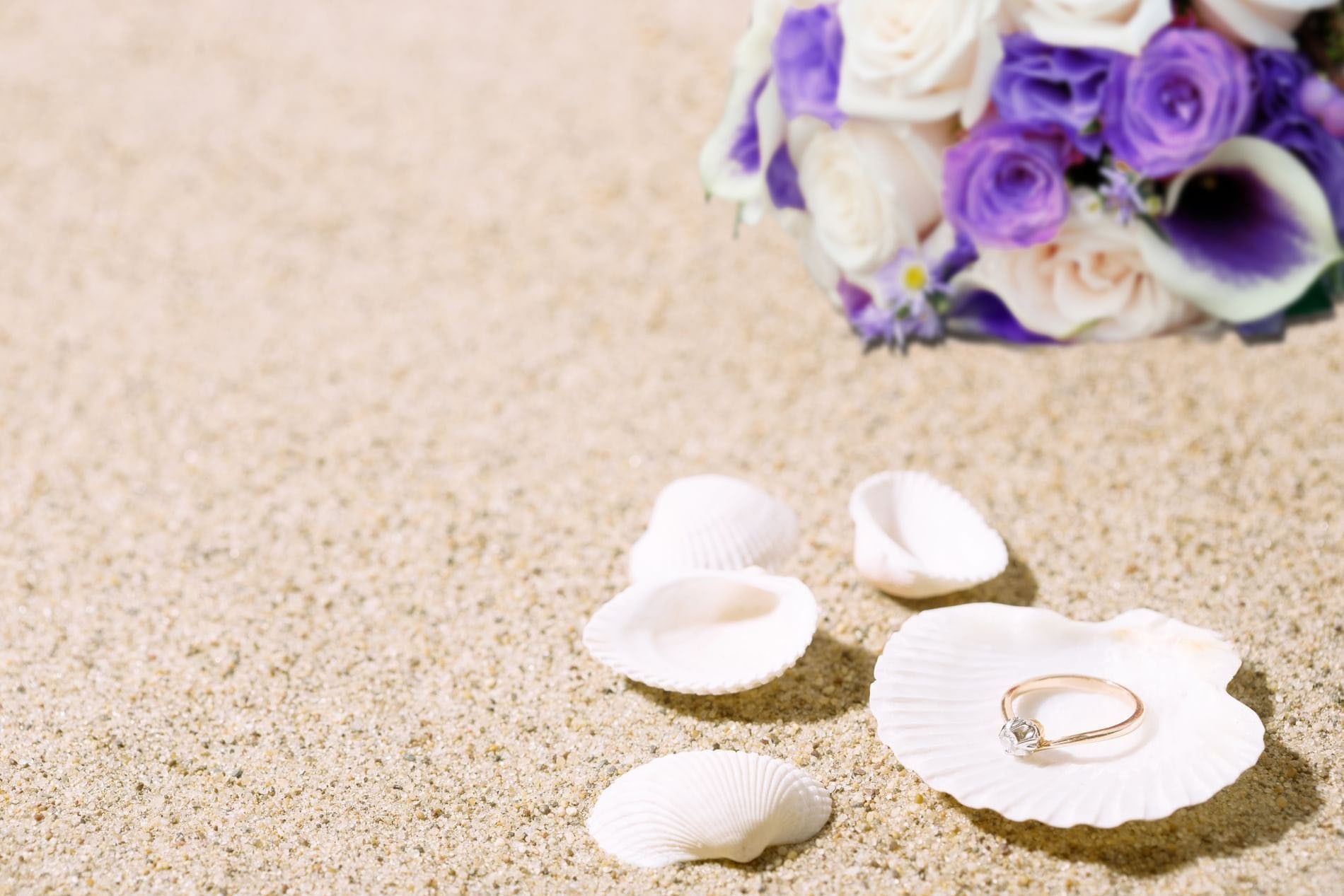 Gold ring in a seashell by a flower bouquet under the sun surrounding beach sand at Warwick Paradise Island Bahamas