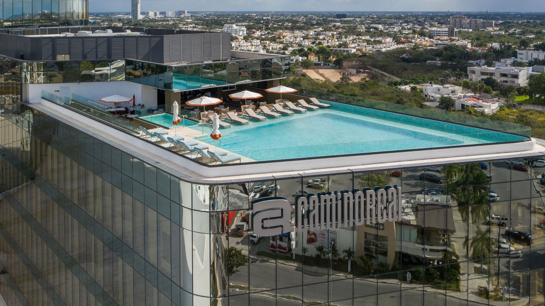 High-angle view of the rooftop pool with umbrellas and a clear view of the city at Camino Real Merida