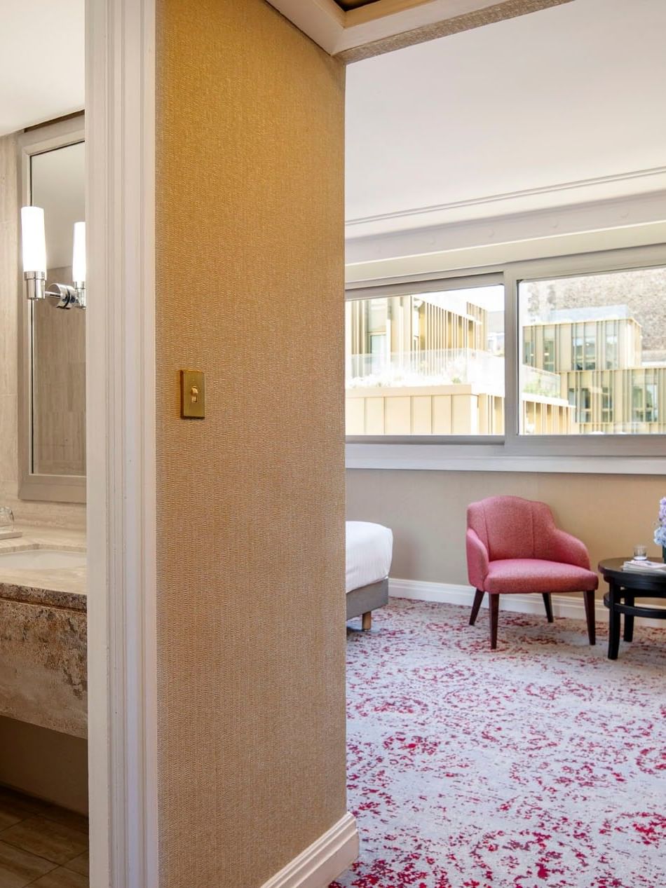 Marble vanity by a bathtub near a bedroom area with a pink chair and desk in Deluxe Room at Warwick Paris Champs Elysées