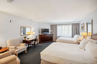 Two beds beside a desk with striped armchairs near a window in the Luxury Room at Avon Old Farms Hotel