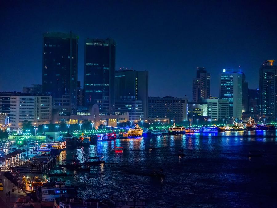 Nighttime cityscape by Dubai Creek with illuminated buildings and boats near DAMAC Hotels & Resorts