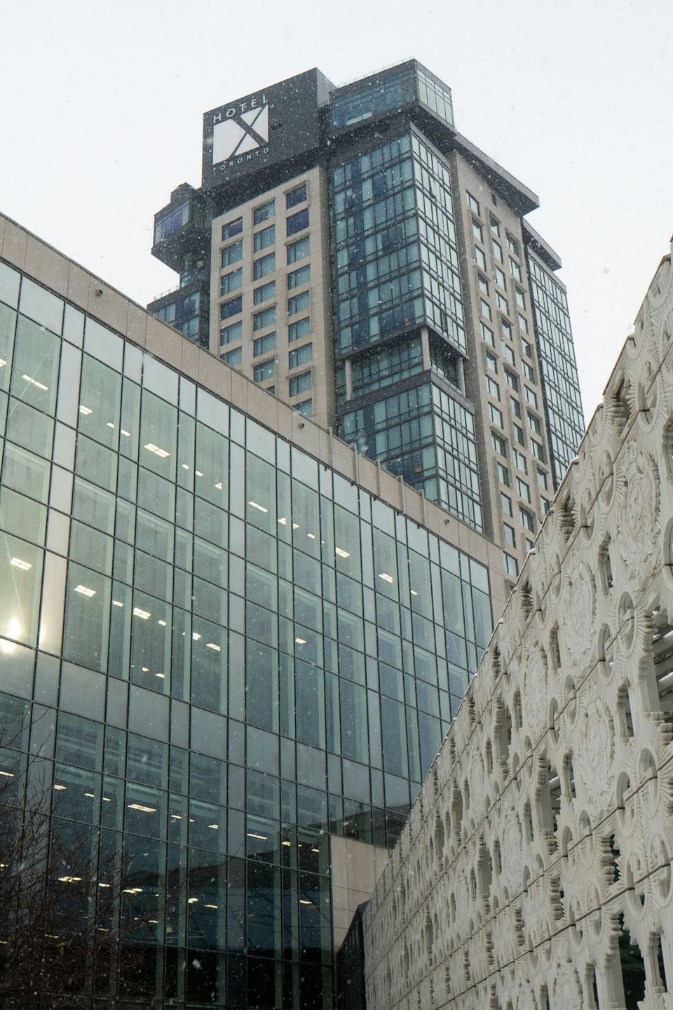 Tall modern hotel building featuring a glass facade and detailed white side wall during snowfall at Hotel X Toronto