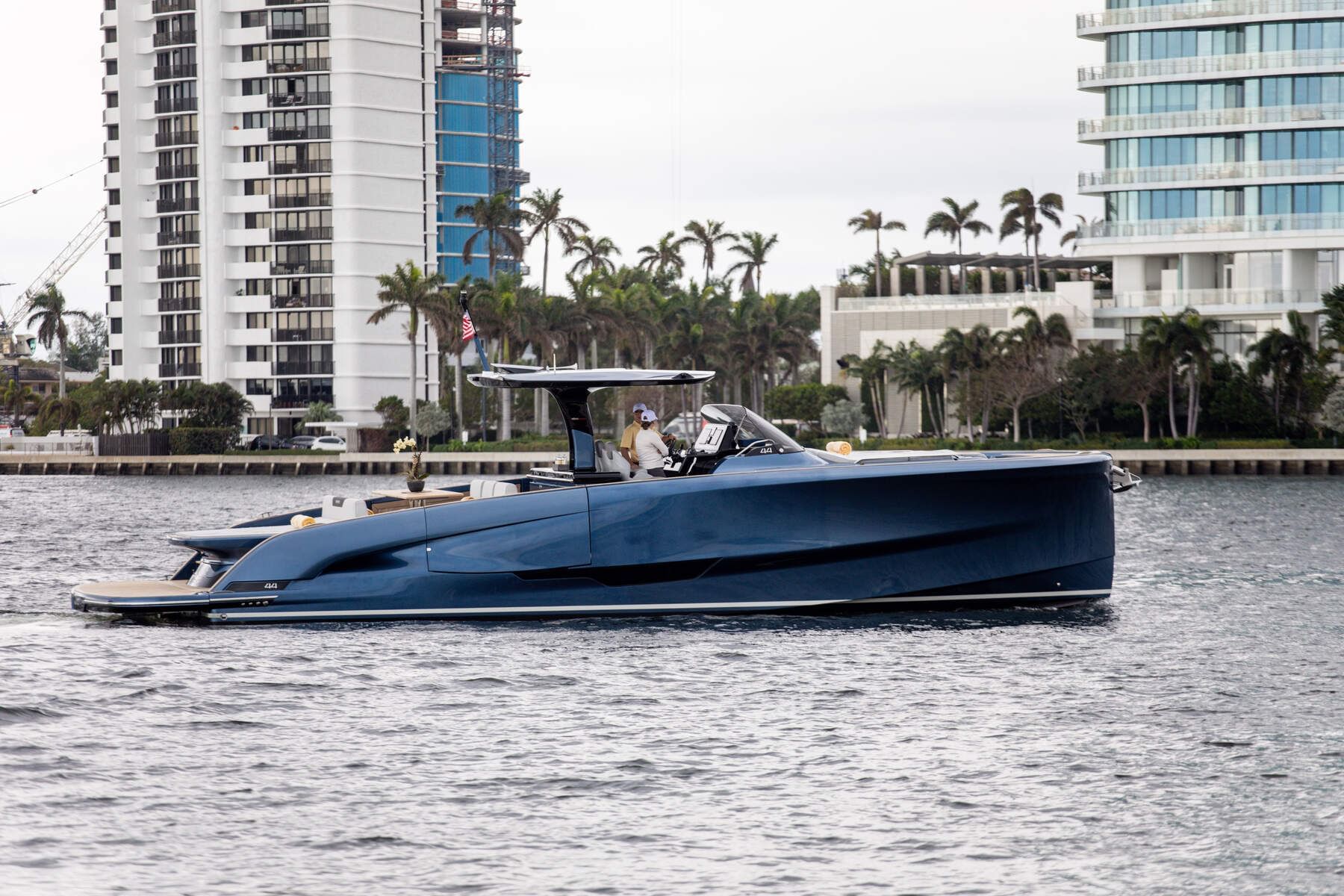 Sleek dark blue BC One yacht cruising along calm water in front of high-rise buildings near The Brazilian Court