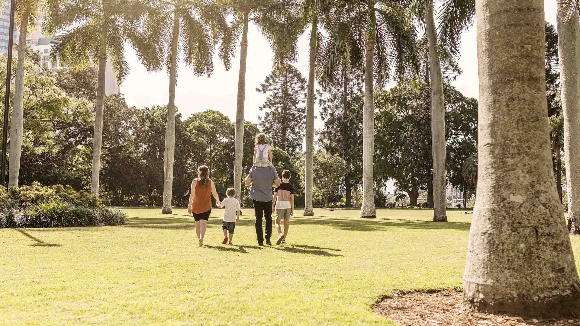 Family of four walking through City Botanic Gardens with tall palm trees on a sunny day near The Sebel Brisbane