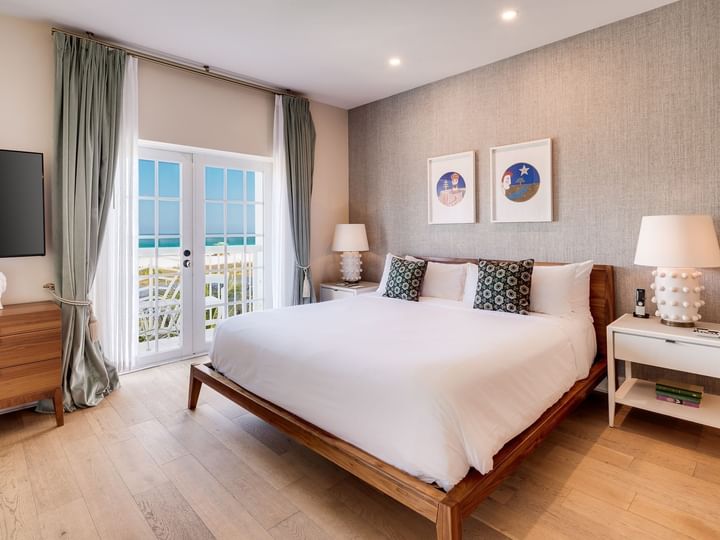 A wide-angle view of a guest room with a large bed, nightstands, and a door leading to an ocean view.
