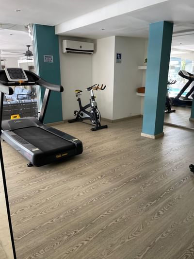 El gimnasio del Country International Hotel cuenta con una cinta de correr y una bicicleta estática sobre suelo de madera clara.