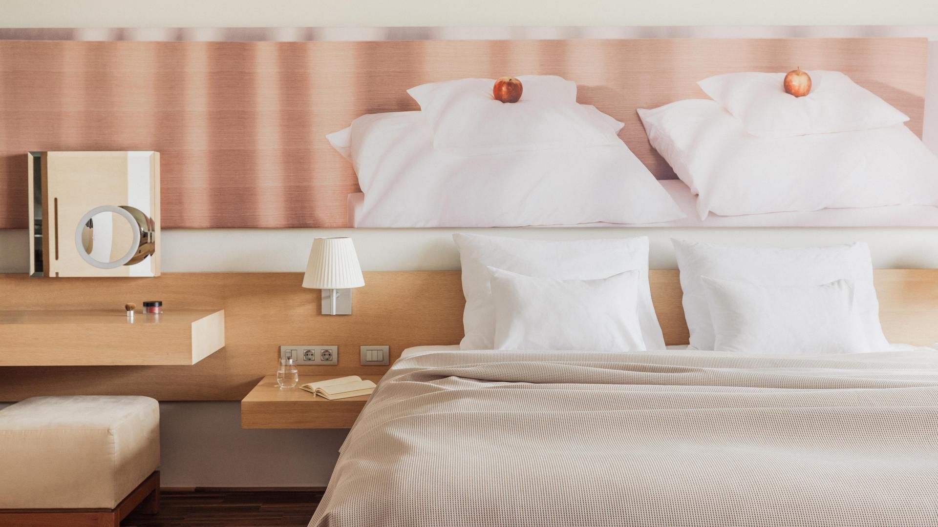 Camera da letto con letto matrimoniale, cuscini, comodini, lampada e grande quadro di cuscini.