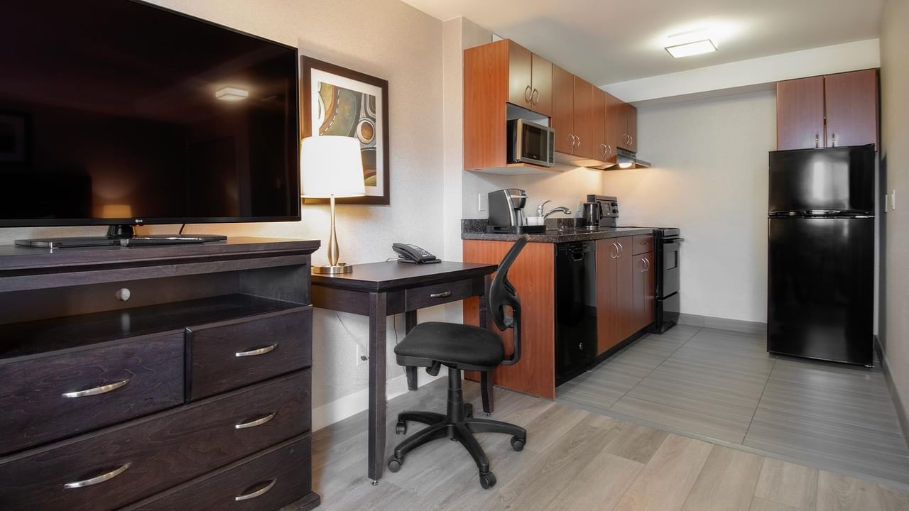 Modern hotel room with a desk, kitchen area, and television.