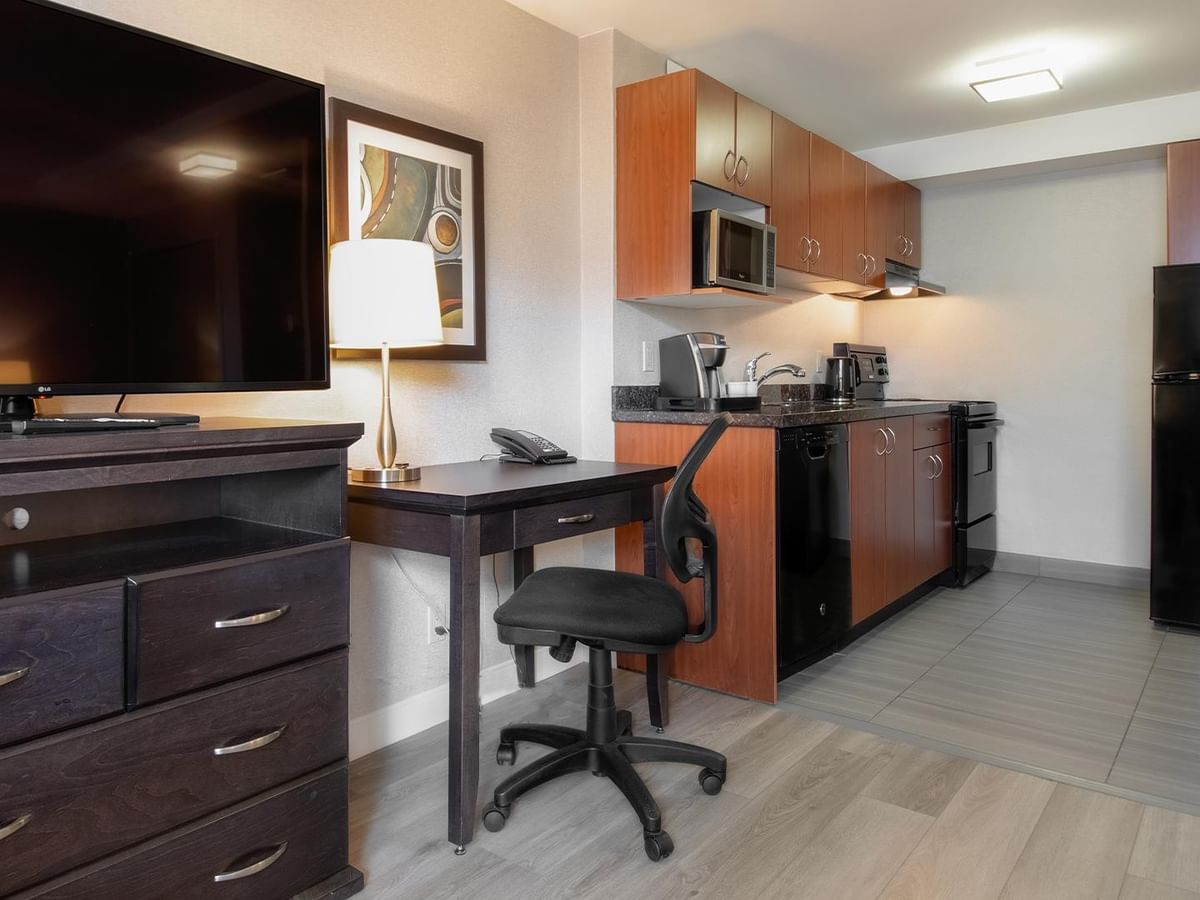 Hotel room with kitchen, desk, and flat-screen TV.