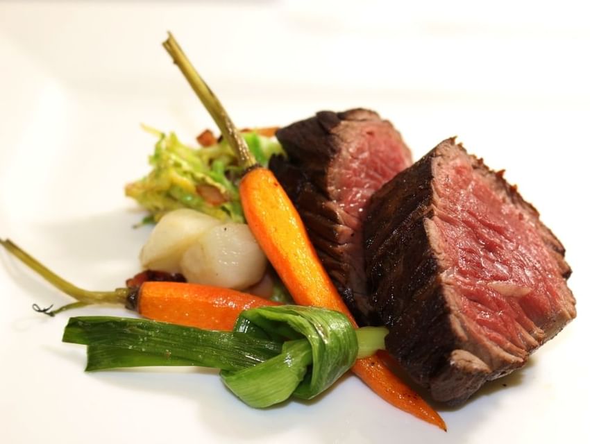 Tender cut of steak plated medium-rare with roasted carrots and sautéed greens served in Tudors Restaurant at Marygreen Manor