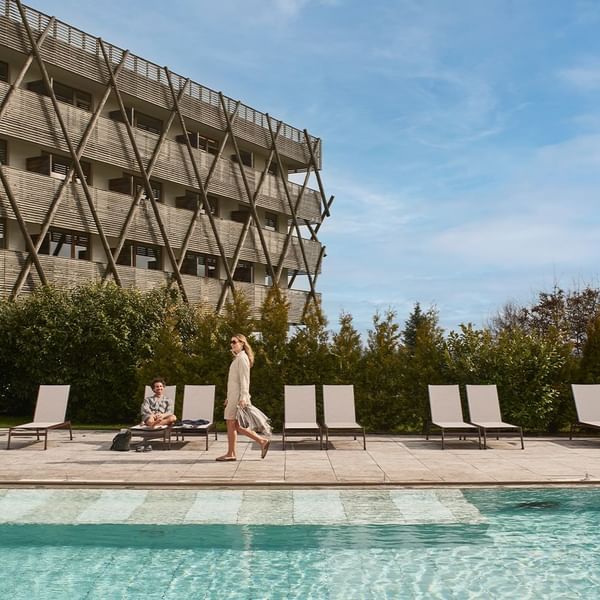 Frau geht am Pool vorbei, während ein Mann auf einer Liege daneben sitzt.