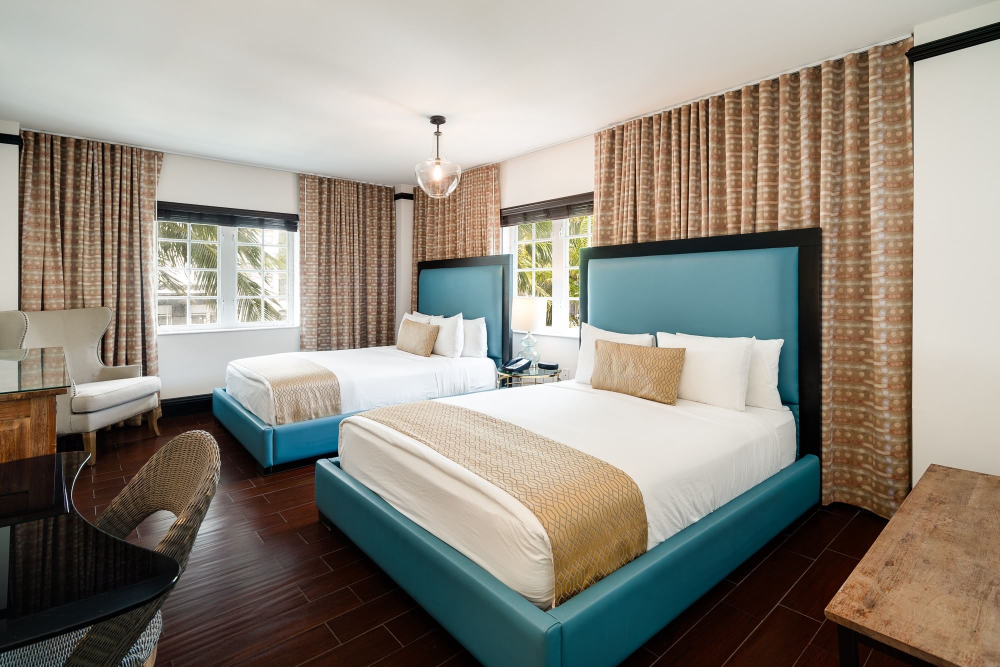 A hotel room with two beds, a tiled floor, and curtained windows.