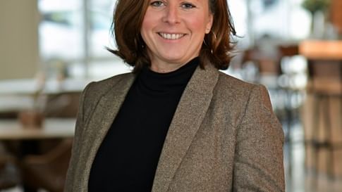 Femme souriante en blazer brun et haut noir à l'Hôtel Rivella.