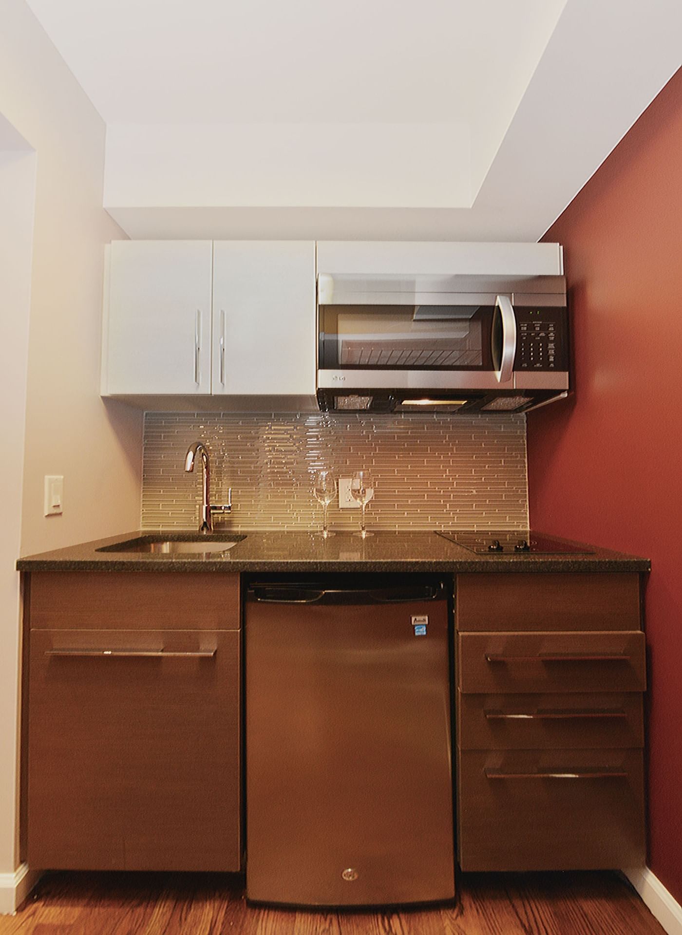 A compact kitchenette with a microwave, sink, refrigerator, and cabinets.