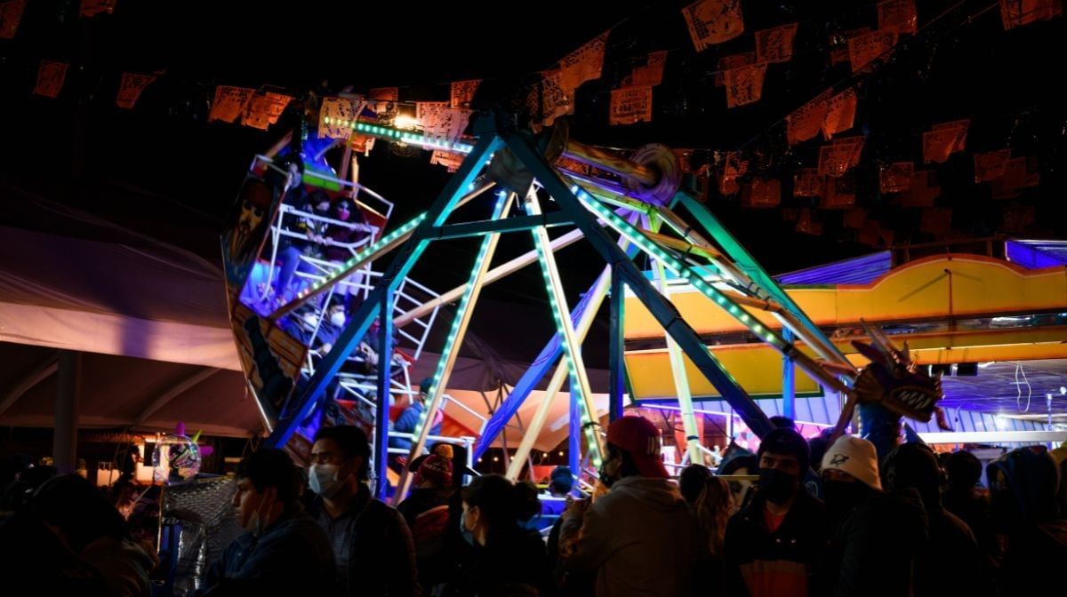 Fair ride with neon lights by a crowd under hanging flags in the night sky at Camino Real Pedregal Mexico