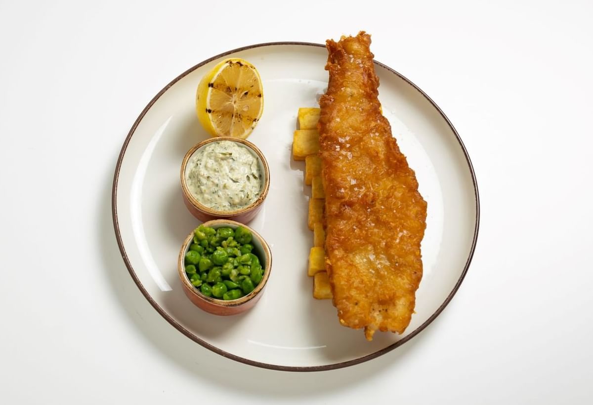 Plate of golden battered fish with mushy peas and a grilled lemon wedge at May Fair Kitchen, The May Fair Hotel