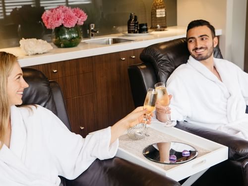 Couple in robes clinking champagne glasses at Stephanies Spa, Sofitel Brisbane Central