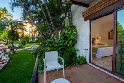 Balcony with white chair, lush greenery, and view of a hotel with pool and lounge chairs.